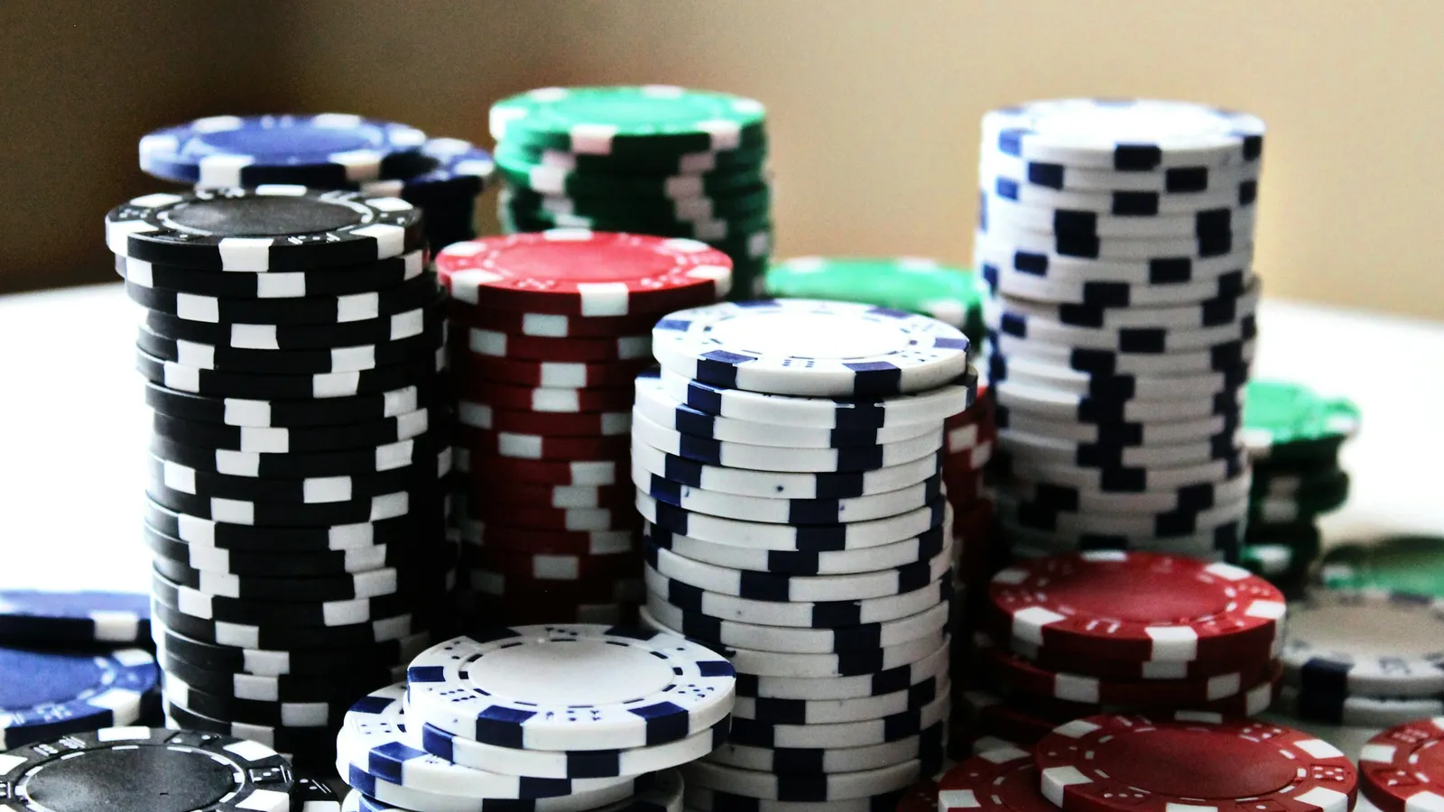 Several stacks of red, black, blue, white and green casino chips standing on a white table against a plain beige wall.