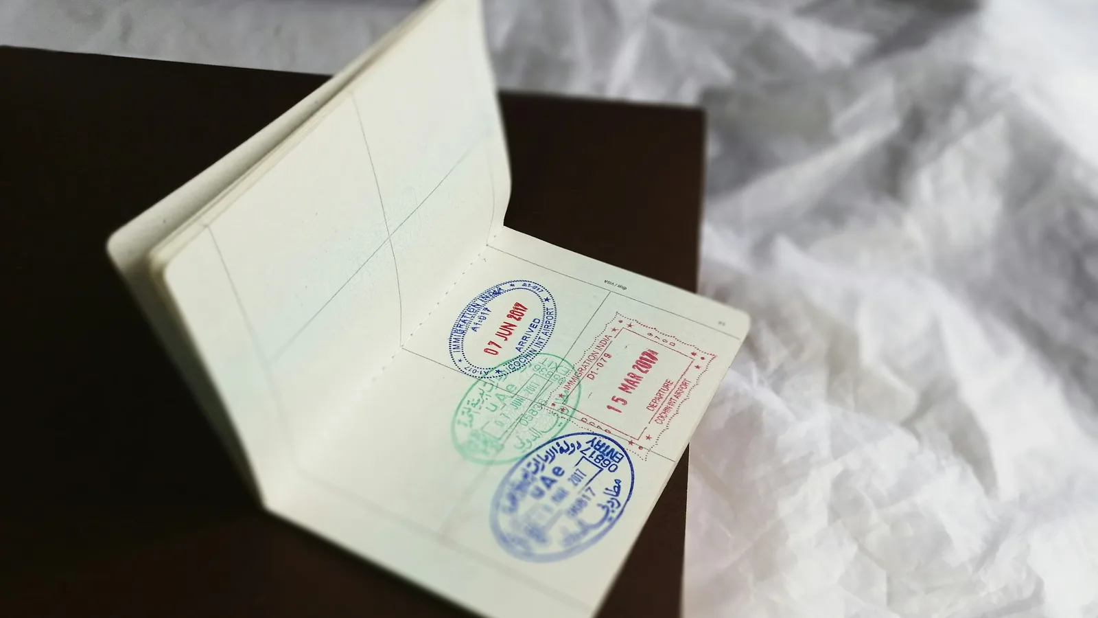 An open passport on a dark surface showing blue, green and red entry and departure stamps on one page.
