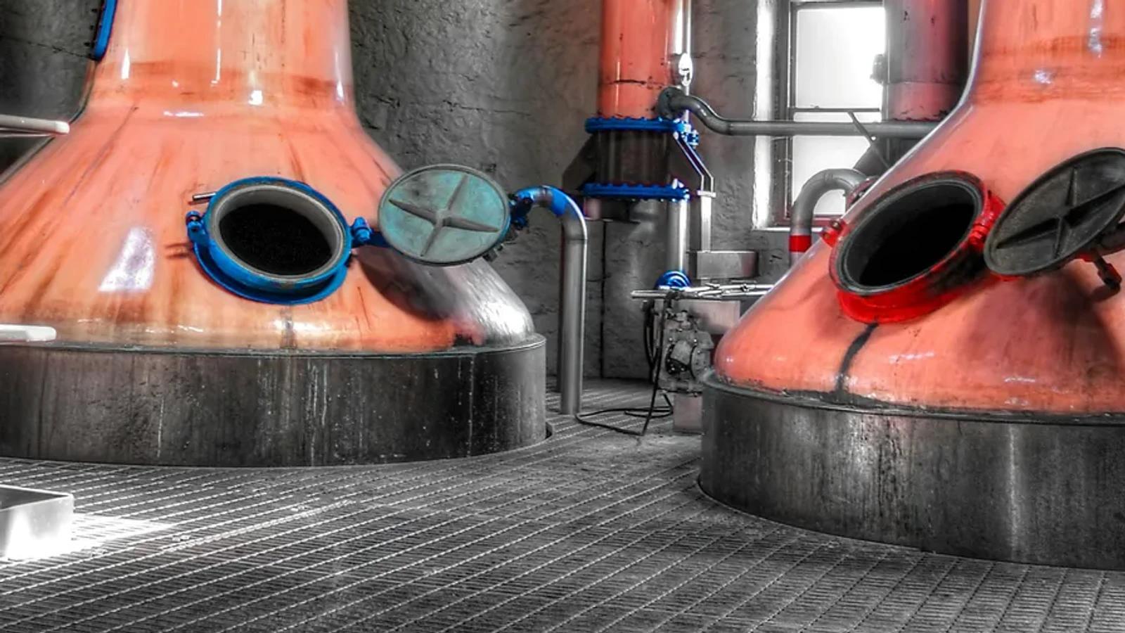 Close-up of two copper stills with open hatches and connecting pipes