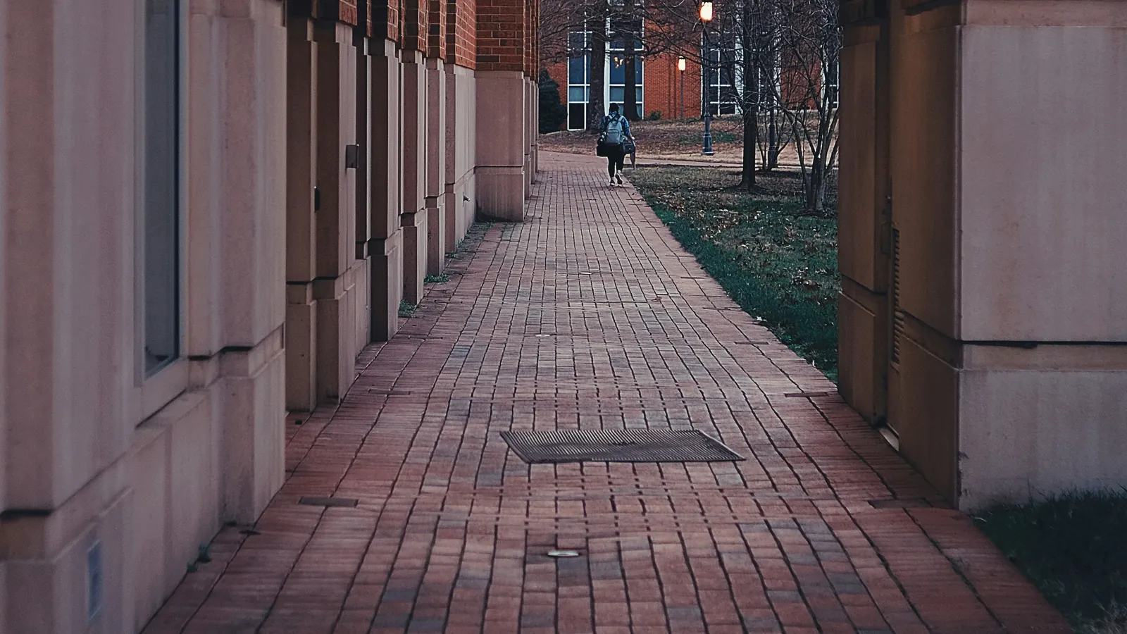 A brick walkway between campus buildings, with one student walking away in the distance.